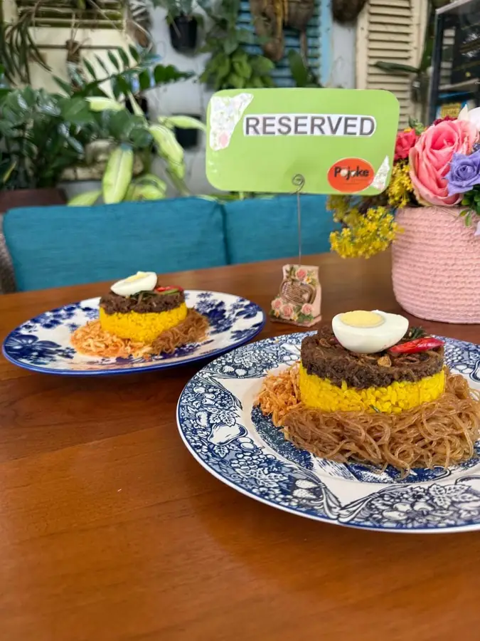 Sajian nasi kuning di atas piring motif biru putih di meja kafe