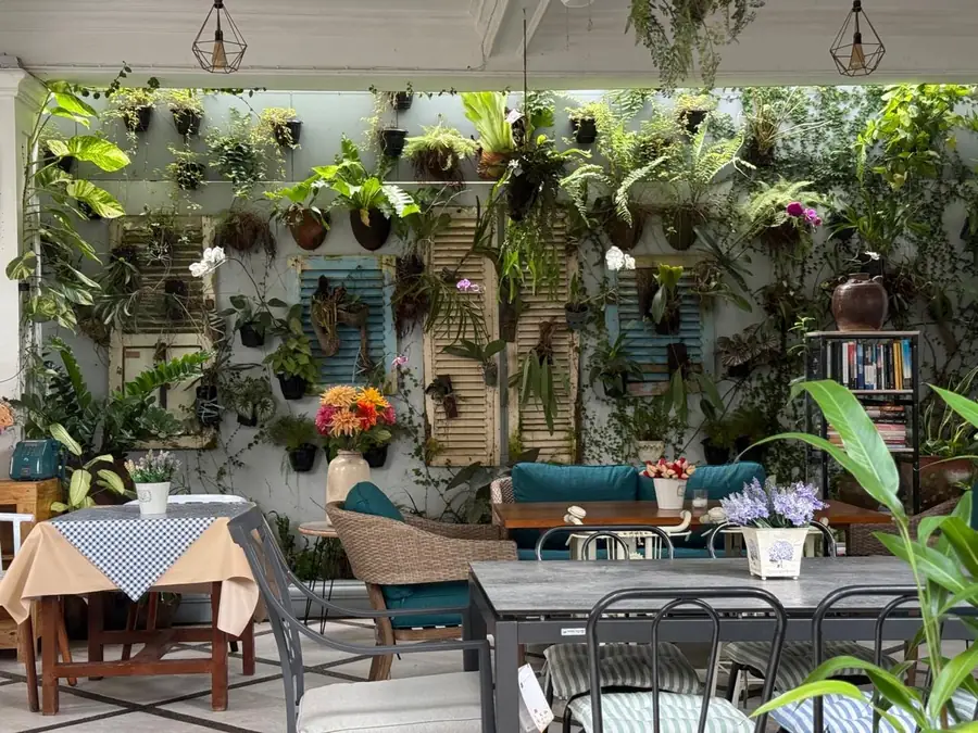 Sudut taman kafe dengan dinding tanaman gantung dan meja berlapis kain kotak-kotak
