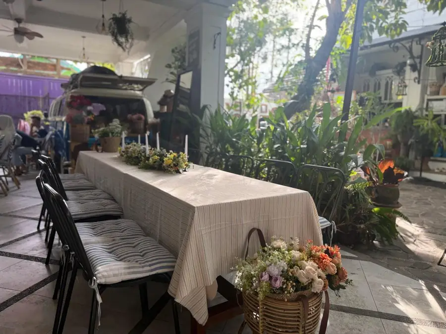 Meja panjang berhias bunga di sisi taman kafe